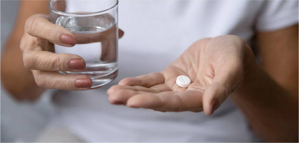 Pacient s osteoporózou drží pohár vody a tabletku.