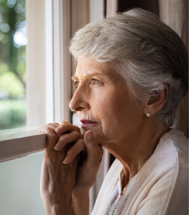 Staršia žena s osteoporózou pozerajúca sa von cez okno.