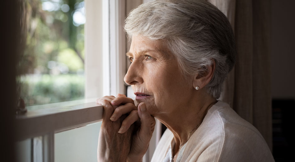 Staršia žena s osteoporózou pozerajúca sa von cez okno.