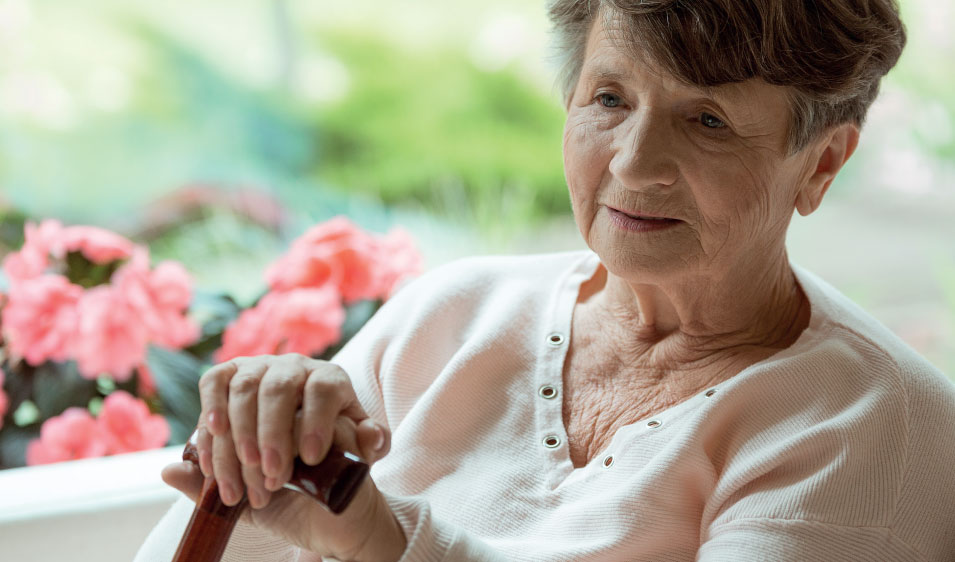 Staršia žena s osteoporózou sediaca na pohovke.